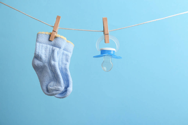 Small socks and pacifier hanging on washing line against color background, space for text. Baby accessories - Фото, зображення