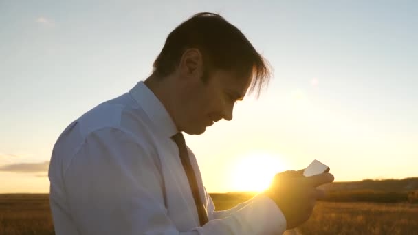 Geschäftsmann, der im Park in den warmen Strahlen des Sonnenuntergangs Tablet-Spiele spielt. Mann spielt Spiele auf dem Smartphone. glücklicher Mann in weißem Hemd und Krawatte spielt online auf Tablet. - Filmmaterial, Video