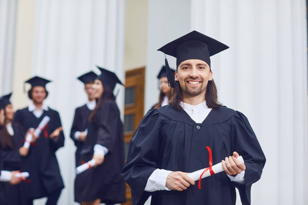 Male graduate is smiling against the background of university graduates. - Φωτογραφία, εικόνα