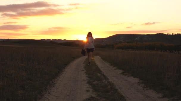 太陽の手でブリーフケースの国の道路に沿って歩くセクシーなビジネスウーマンは日没でゆらめきます。田舎で働くセクシーなビジネス女性。美しい少女は、田舎を旅します。. - 映像、動画