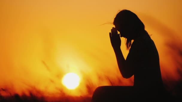 Silhouette of a woman praying against the background of an orange sky and a large setting sun - Footage, Video
