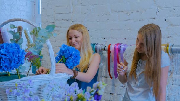 Две женщины-флористки делают большую цветочную корзину с цветами в цветочном магазине - Фото, изображение