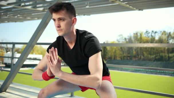 A Young Man Doing Stretching On A Mat In The Open Air Near The Stadium. He Does Yoga Exercises On A Blue Mat. Dressed In Red Shorts And A Black T-Shirt. The Concept Sorowako Lifestyle And Sports - Záběry, video