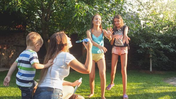 Photo of happy laughing children blowing and cathcing soap bubbles at house backyard. Family playing and having fun outdoors at summer - Φωτογραφία, εικόνα