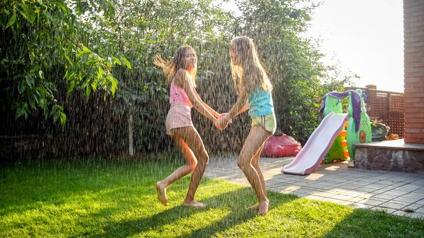 Kuva onnellisista nauravista lapsista märissä vaatteissa hyppäämässä ja tanssimassa lämpimässä sateessa puutarhassa. Perhe leikkii ja pitää hauskaa ulkona kesällä
 - Valokuva, kuva