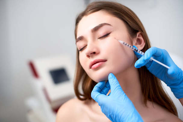 Beautician doctor with botulinum toxin syringe making injection to to remove crows feet. Cheek volume enhance mesotherapy. Anti-aging treatment and face lift in cosmetology clinic. - Fotografie, Obrázek
