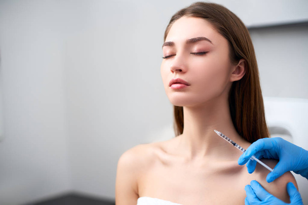 Beautician doctor with botulinum toxin syringe making injection to platysmal bands. Neck rejuvenation mesotherapy. Anti-aging treatment and face lift in cosmetology clinic. Patient lying on chair. - 写真・画像