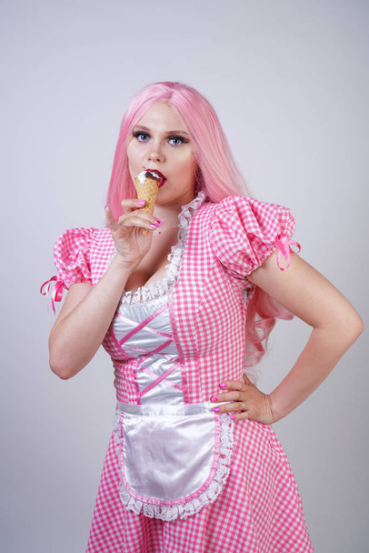 chica gordita caucásica erótica en vestido de muñeca a cuadros rosa sostiene delicioso helado de verano y coquetea sexy sobre fondo de estudio blanco
 - Foto, Imagen