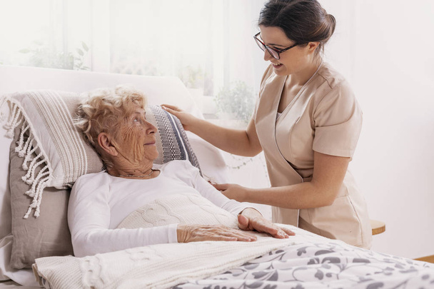 Elderly woman in hospital bed with social worker helping her - Foto, Imagen