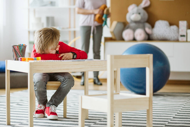 Cute little boy wearing red sweater sitting at small wooden table - Fotoğraf, Görsel