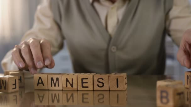Elderly pensioner making word amnesia of wooden cubes on table, health care - Filmati, video