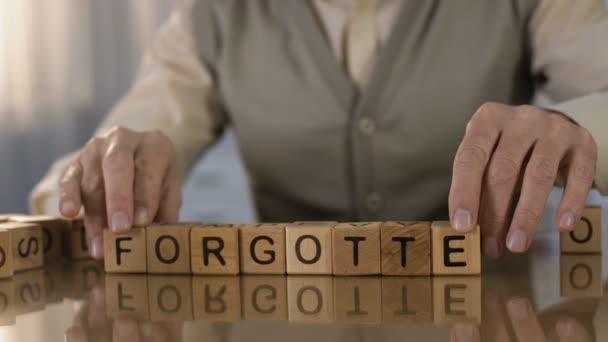 Elderly male making word forgotten of wooden cubes on table, dementia disorder - Video, Çekim