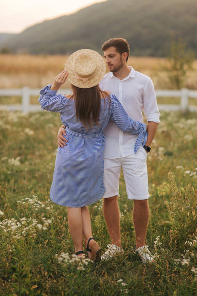 Man en zijn zwangere vrouw staan in het veld in de buurt van de boerderij en knuffelen elkaar - Foto, afbeelding