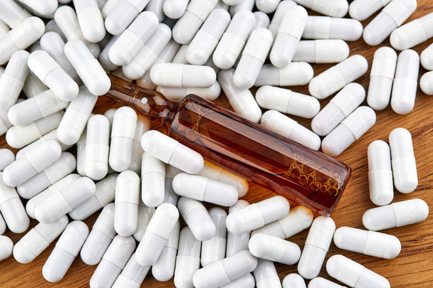 Many white pills and brown ampoule on wooden background - Photo, Image