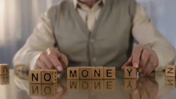 Mature man making words no money of wooden cubes on table, pension age poverty - Séquence, vidéo