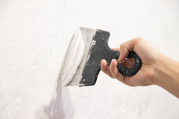 Mano masculina con una espátula aplicando masilla en la pared. Reparación apartamento
 - Foto, Imagen