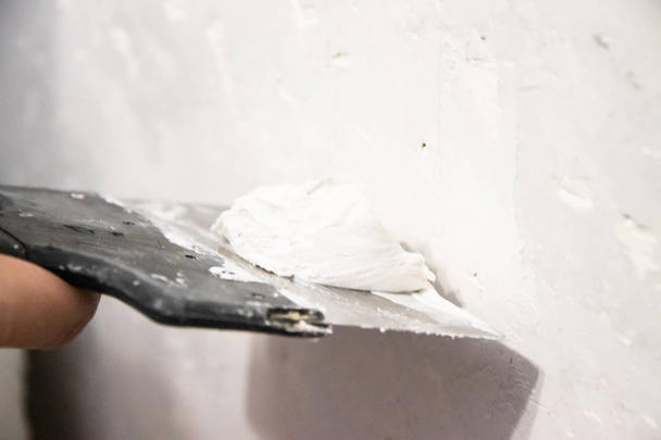 Mano masculina con una espátula aplicando masilla en la pared. Reparación apartamento
 - Foto, imagen