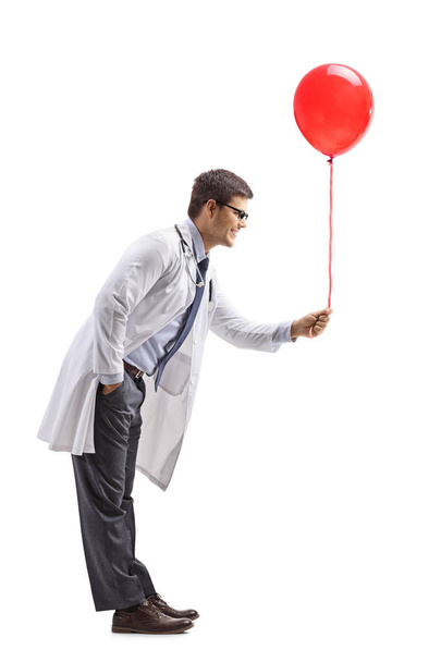Full length profile shot of a male doctor giving a red balloon isolated on white background - Foto, Bild