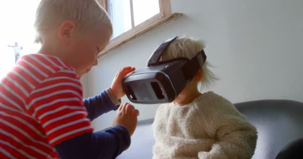 Side view of Caucasian siblings using virtual reality headset in living room at home. They are sitting on sofa 4k - Materiaali, video
