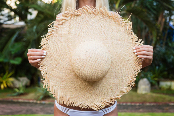 Closeup portrait of young woman holding big straw hat, beautiful female enjoying tropical sunny weather - Фото, изображение