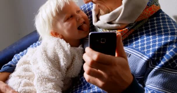 Előnézete kaukázusi apja és fia vesz selfie mobiltelefonnal a nappaliban otthon. Ezek a szórakozás 4k - Felvétel, videó