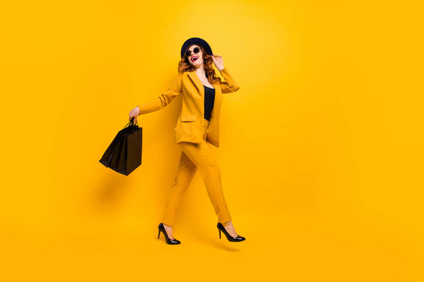 Full length side profile body size photo beautiful she her lady walking down street carry new clothes packs perfect look traveler wear specs formal-wear costume suit isolated yellow bright background - Fotó, kép