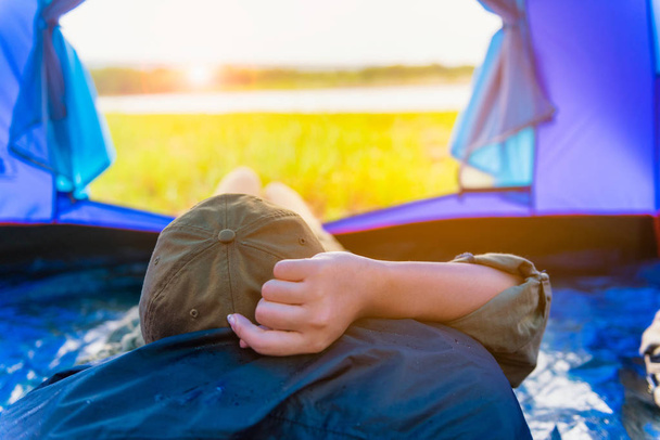 Mujer joven acostada en tienda de campaña o durmiendo en el bolso con una vista al atardecer en las montañas y el lago, Camping con puesta de sol en el campamento base, Una actividad Relajante en verano
 - Foto, imagen
