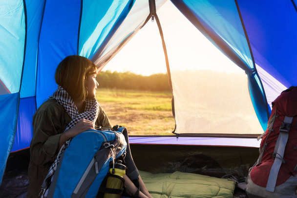 Donna seduta all'interno della tenda da campeggio blu che guarda verso il tramonto. Attività rilassanti campeggio nella foresta o nel parco di montagna
. - Foto, immagini