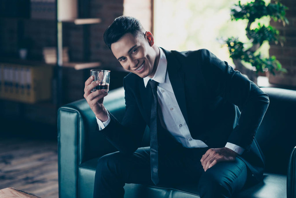Close up photo handsome he him his perfect white teeth hands arms whisky beverage enjoy pause break toasting wear formal-wear dress code shirt jacket tie suit costume sit chair indoors office place - 写真・画像