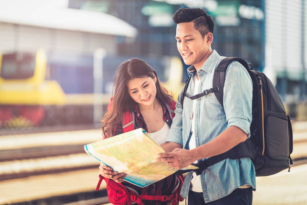 若いカップルアジア地図を保持し、場所の地図上の方向を検索します。暖かい日差しを背景に駅での旅行を楽しんでください。列車のコンセプトで一人でアウトドアアドベンチャー旅行. - 写真・画像