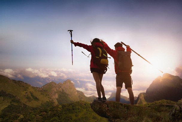 zwei Wanderer mit Rucksäcken stehen zum Verweilen auf einem Berg und genießen den Blick auf den Nebel im Tal bei Sonnenaufgang. - Foto, Bild