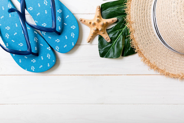 麦わら帽子、緑の葉、青いフリップフロップとヒトデ白い木製の背景に。コピースペース付きのトップビュー夏休みコンセプト - 写真・画像