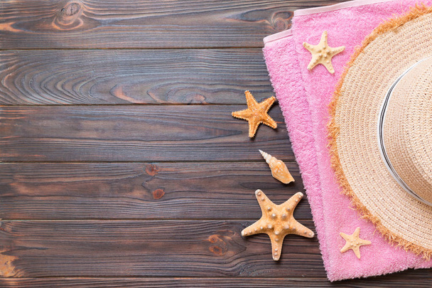Kapelusz Słomkowy, różowy ręcznik i rozgwiazdy na ciemnym drewnianym tle. Top View lato koncepcja wakacje z kopią - Zdjęcie, obraz