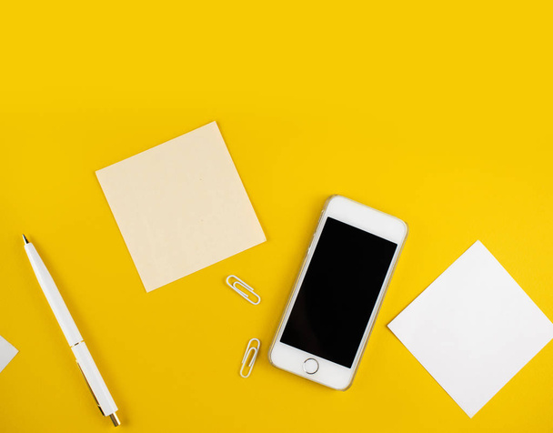 Minimalistic workplace concept, with a smartphone, pen and business work records on a yellow background. Image digital agency, online education. Top view. Flat lay style. - Valokuva, kuva