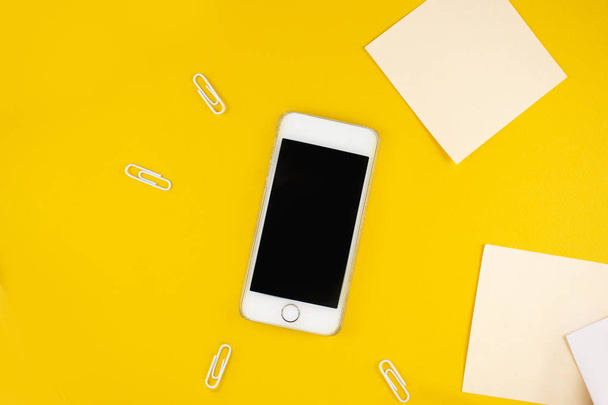 Minimalistic workplace concept, with a smartphone, pen and business work records on a yellow background. Image digital agency, online education. Top view. Flat lay style. - Фото, изображение