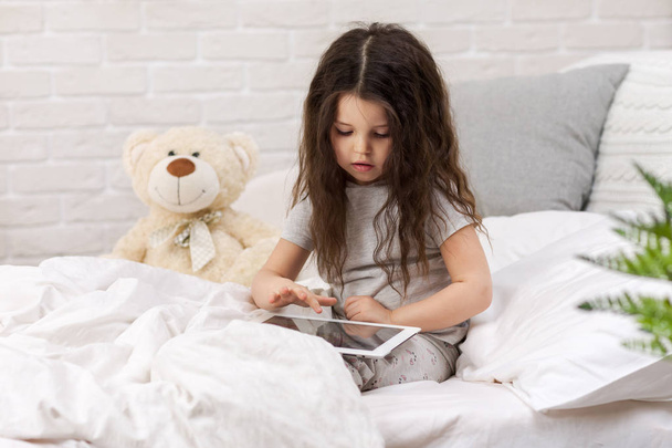 cute little girl lies in bed uses digital tablet. - Fotó, kép