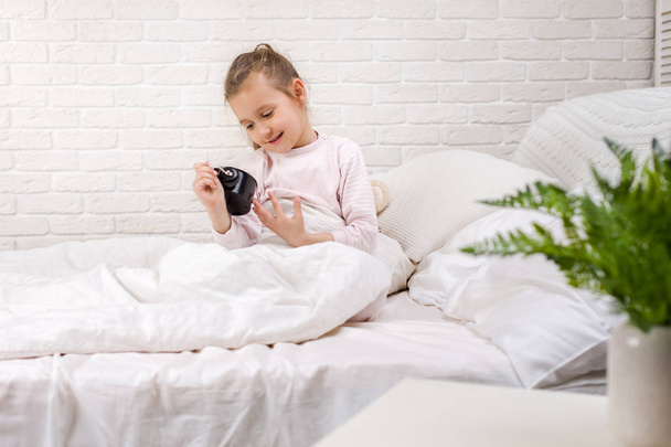 Little girl in pyjamas with clock - Valokuva, kuva