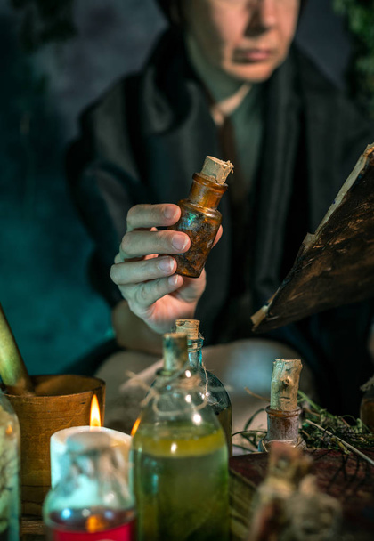 Bruja oscura en el trabajo: la mujer mágica negra hace la brujería mezclando hierbas, lanzando hechizos, ejecutando rituales mágicos - Foto, imagen