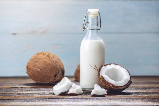 Кокосовое молоко в бутылке с белой плотью на деревянном фоне. Органический здоровый продукт, используемый в косметологии
 - Фото, изображение