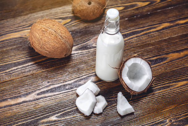 Kokosové mléko v láhvi s bílým masem na dřevěném podkladu. Ekologicky zdravý produkt používaný v kosmetologii - Fotografie, Obrázek