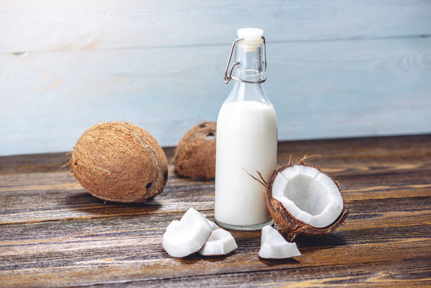 Kokosmilch in einer Flasche mit weißem Fruchtfleisch auf einem hölzernen Hintergrund. Gesundes biologisches Produkt in der Kosmetologie - Foto, Bild
