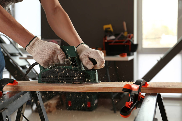 Плотник-мужчина с помощью электрического планера в мастерской
 - Фото, изображение