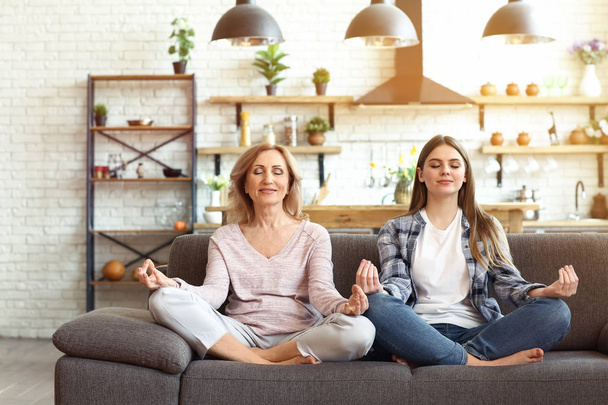 Happy mother and daughter meditating on sofa at home - Photo, Image