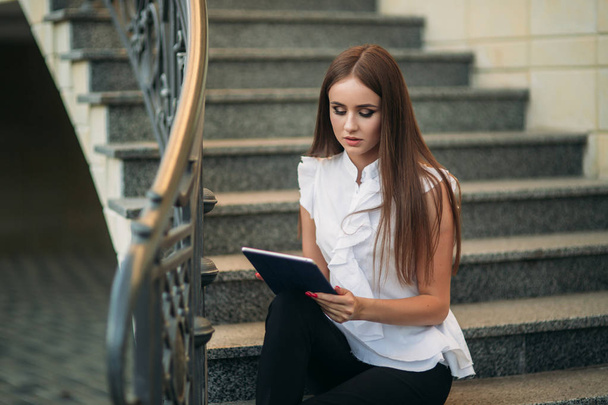 Joven y atractiva hembra sittind en las escaleras y utilizar la tableta. Mujer jugar juegos en línea en la tableta
 - Foto, Imagen