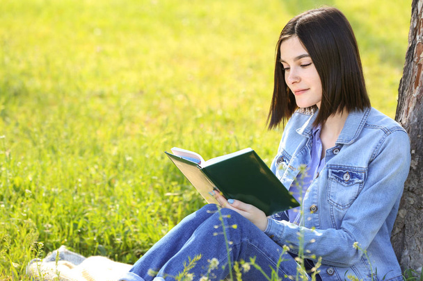 Beautiful young woman reading book in park - Zdjęcie, obraz