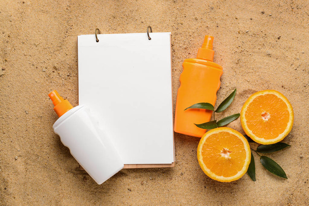 Zonwering crème met notitieboekje en sinaasappel vrucht op zand - Foto, afbeelding