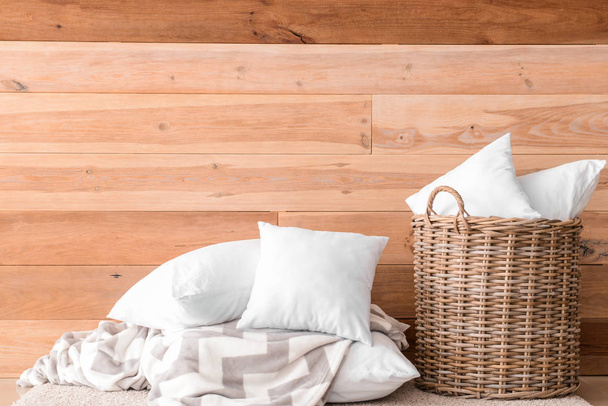 Miękkie poduszki i kosz na podłodze przed drewnianą ścianą - Zdjęcie, obraz