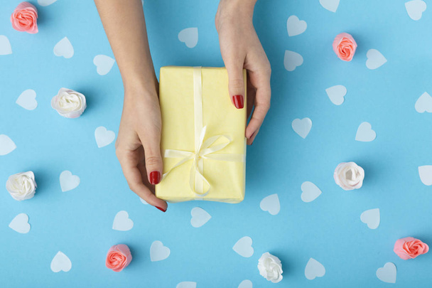 female hands with a gift box on a pastel colored blue background top view, the girl holding a present with decorations, the concept of holidays and love - Photo, Image