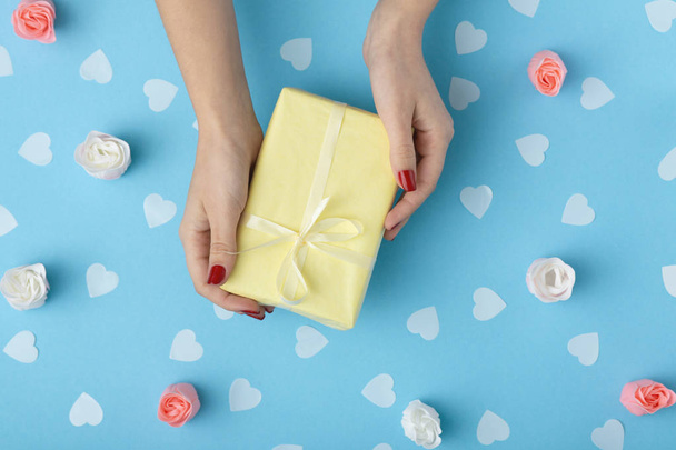 female hands with a gift box on a pastel colored blue background top view, the girl holding a present with decorations, the concept of holidays and love - Foto, afbeelding