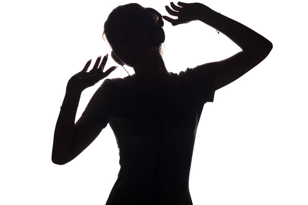 Silhouette eines glücklichen Mädchens, das Musik über Kopfhörer hört, Gestalt einer jungen Frau mit erhobenen Händen, die sich auf einem weißen, isolierten Hintergrund entspannt und zur Musik tanzt - Foto, Bild